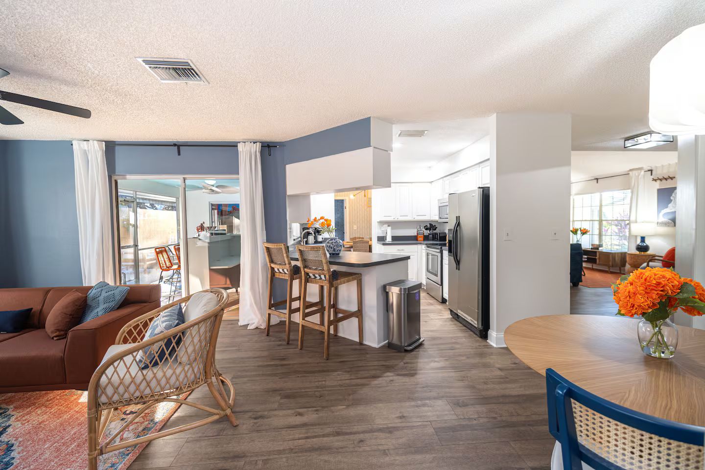 A modern kitchen with a central island, bar stools, and a stainless steel refrigerator.