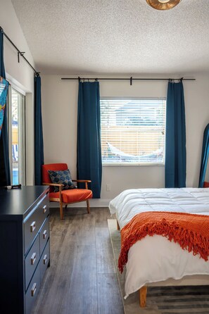 A bedroom with a bed, a chair, a dresser, and a window with curtains. - Palm Harbor Heated Pool Resort - Theater Mini Golf (Palm Harbor)