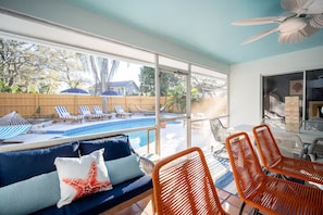 Ein Zimmer mit Blick auf einen Swimmingpool, einem Deckenventilator und einer Sitzecke mit einer Couch und Sesseln.