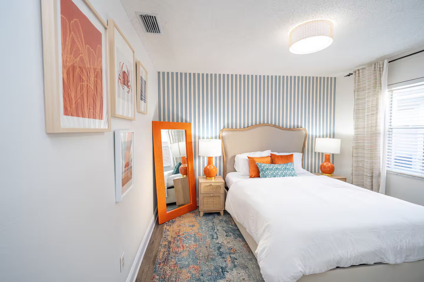 Une chambre d’hôtel avec un lit, des tables de chevet, des lampes, un miroir et un papier peint à rayures.