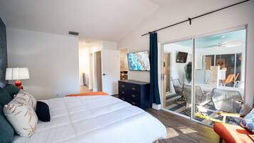 Habitación de hotel con cama, televisión, escritorio y balcón con sillas.