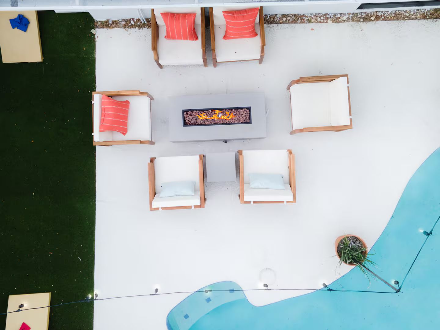 A top-down view of a poolside area with lounge chairs and a table, surrounded by a white deck and a pool.