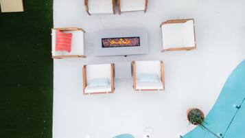 A top-down view of a poolside area with lounge chairs and a table, surrounded by a white deck and a pool.