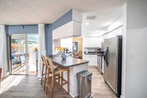 A modern kitchen with a central island, wooden chairs, a stainless steel refrigerator, and a sliding glass door leading to an outdoor area. - Palm Harbor Heated Pool Resort - Theater Mini Golf (Palm Harbor)