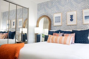 Ein Hotelzimmer mit einem großen Bett, vielen Kissen, einem Spiegel und gerahmten Kunstwerken an der Wand.