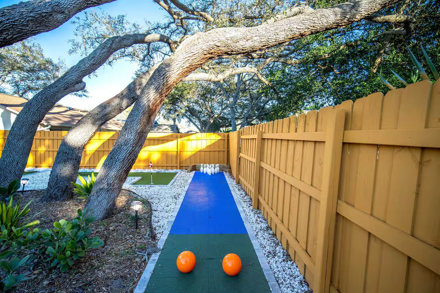 A backyard with a blue mat, two orange balls, a wooden fence, and trees.