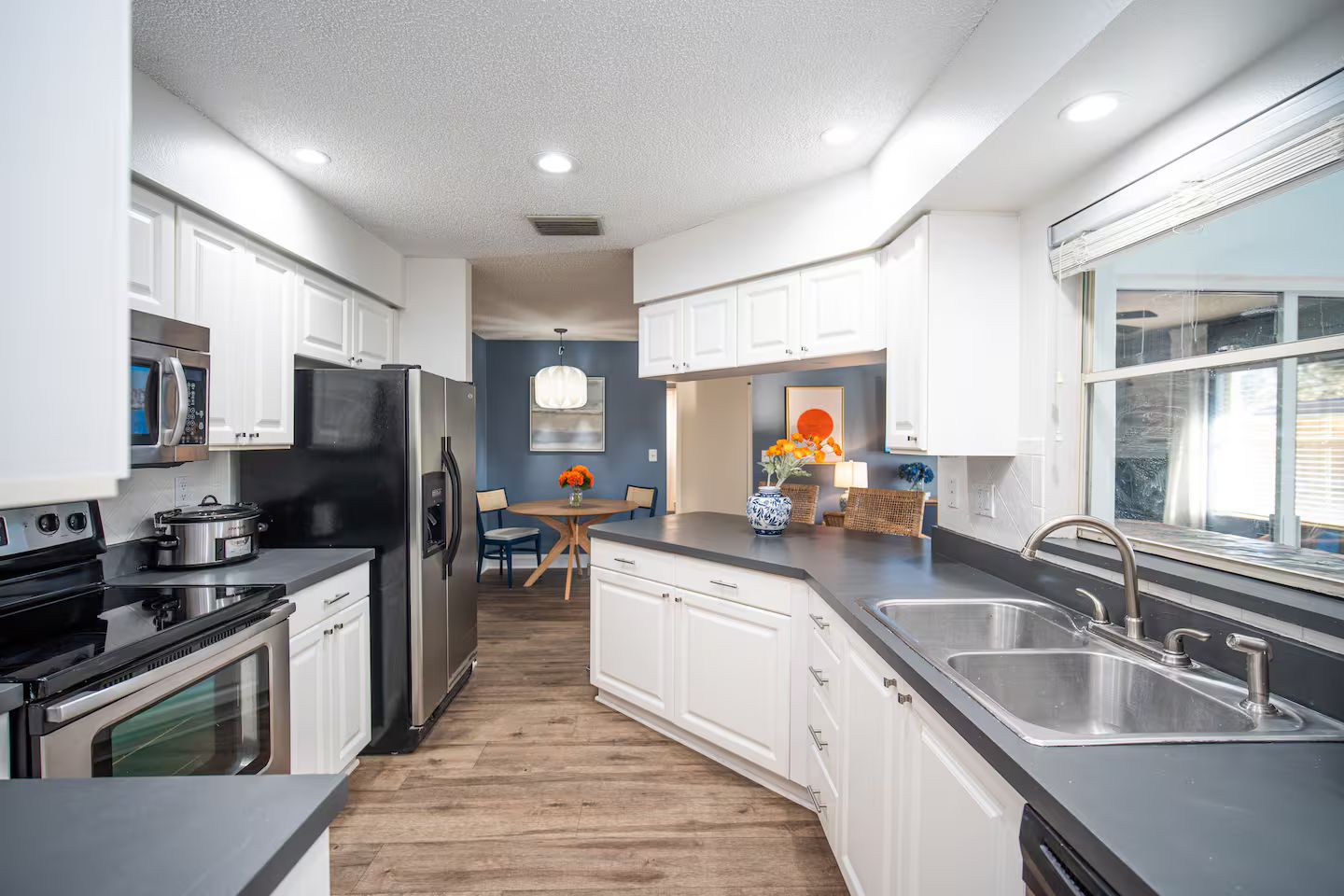 A modern kitchen with white cabinets, stainless steel appliances, and a wooden floor.