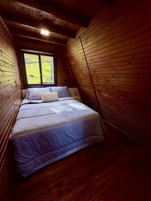 A small, sloped-roofed room with wooden walls and a single bed with a blue bedspread.