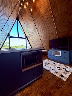 Une cuisine moderne dotée d’un four et d’un micro-ondes encastrés, d’un meuble bleu avec un téléviseur, et d’une grande fenêtre offrant une vue sur l’extérieur.