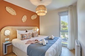 A hotel room with a large bed, a bedside table, a nightstand, a window with curtains, and a ceiling light fixture. - Royan : appartement de prestige en bord de mer (Royan)
