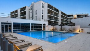 Um hotel moderno com piscina, espreguiçadeiras e um edifício de vários andares com varandas.