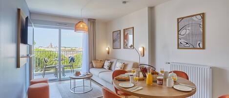 Una sala de estar moderna con comedor, un sofá, una mesa de centro y un balcón con mobiliario exterior.