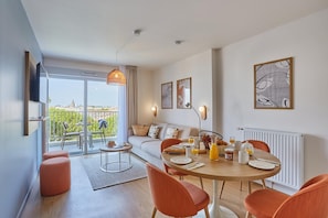 A modern living room with a dining area, a sofa, a coffee table, and a balcony with outdoor furniture. - Royan : appartement de prestige en bord de mer (Royan)