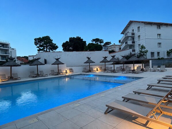 A swimming pool with lounge chairs and umbrellas, surrounded by a building with multiple floors and balconies. - Royan : appartement de prestige en bord de mer (Royan)