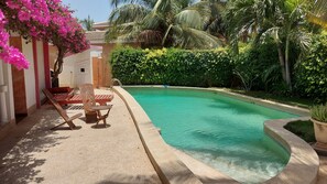 A swimming pool with a curved edge, surrounded by lush greenery and palm trees. - Vrbo Property (M'bour)