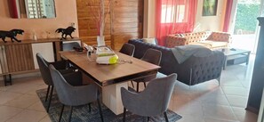 Ein Essbereich mit Holztisch, grauen Stühlen, einer Couch und einer Wand mit Spiegel und zwei Figuren.