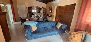 Ein Wohnzimmer mit einem blauen Sofa, einem Esstisch mit St ühlen und einer Küche im Hintergrund.