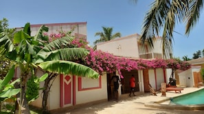 A residential area with a swimming pool, a covered walkway with pink flowers, and a building with a cross. - CHRISTALLINES VILLA RESIDENCE (M'bour)