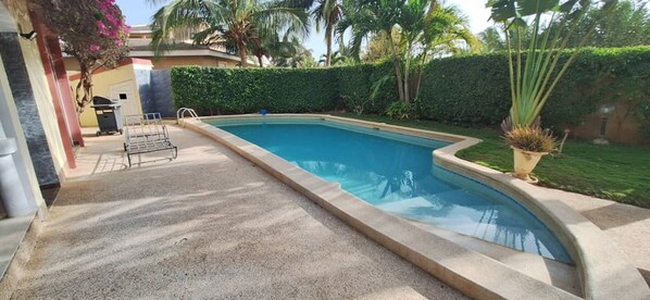 A swimming pool with a concrete deck, surrounded by a well-maintained hedge and palm trees. - Vrbo Property (M'bour)
