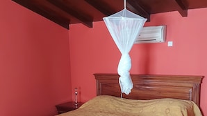 Une chambre avec un lit en bois, une moustiquaire suspendue et un climatiseur fixé au mur.