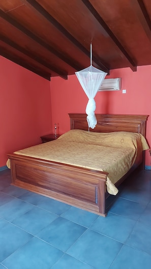 A bedroom with a wooden bed, a hanging mosquito net, and a wall-mounted air conditioner. - Vrbo Property (M'bour)