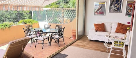 A room with a glass door leading to a patio, a white sofa, a small table, and a wall with framed artwork.