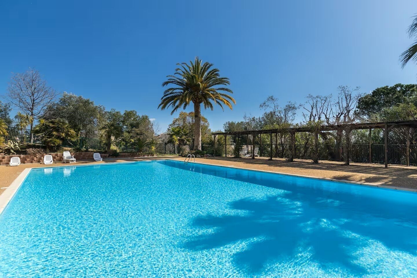 Piscina azul cristalina con sillas de descanso y una pérgola.