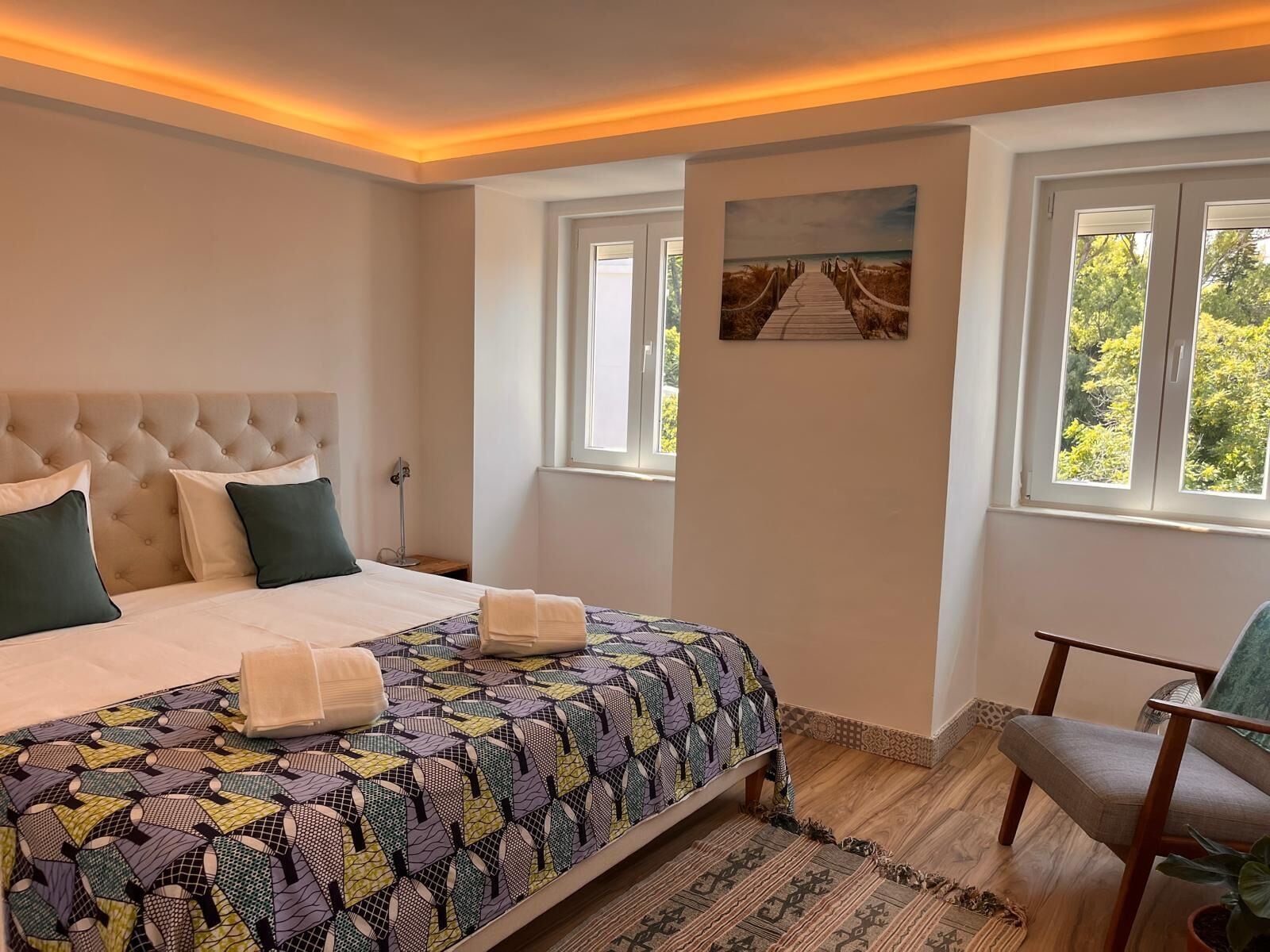 Ein Schlafzimmer mit einem großen Bett, einer Kopfteil, einem Fenster mit Blick und einem Gemälde an der Wand.
