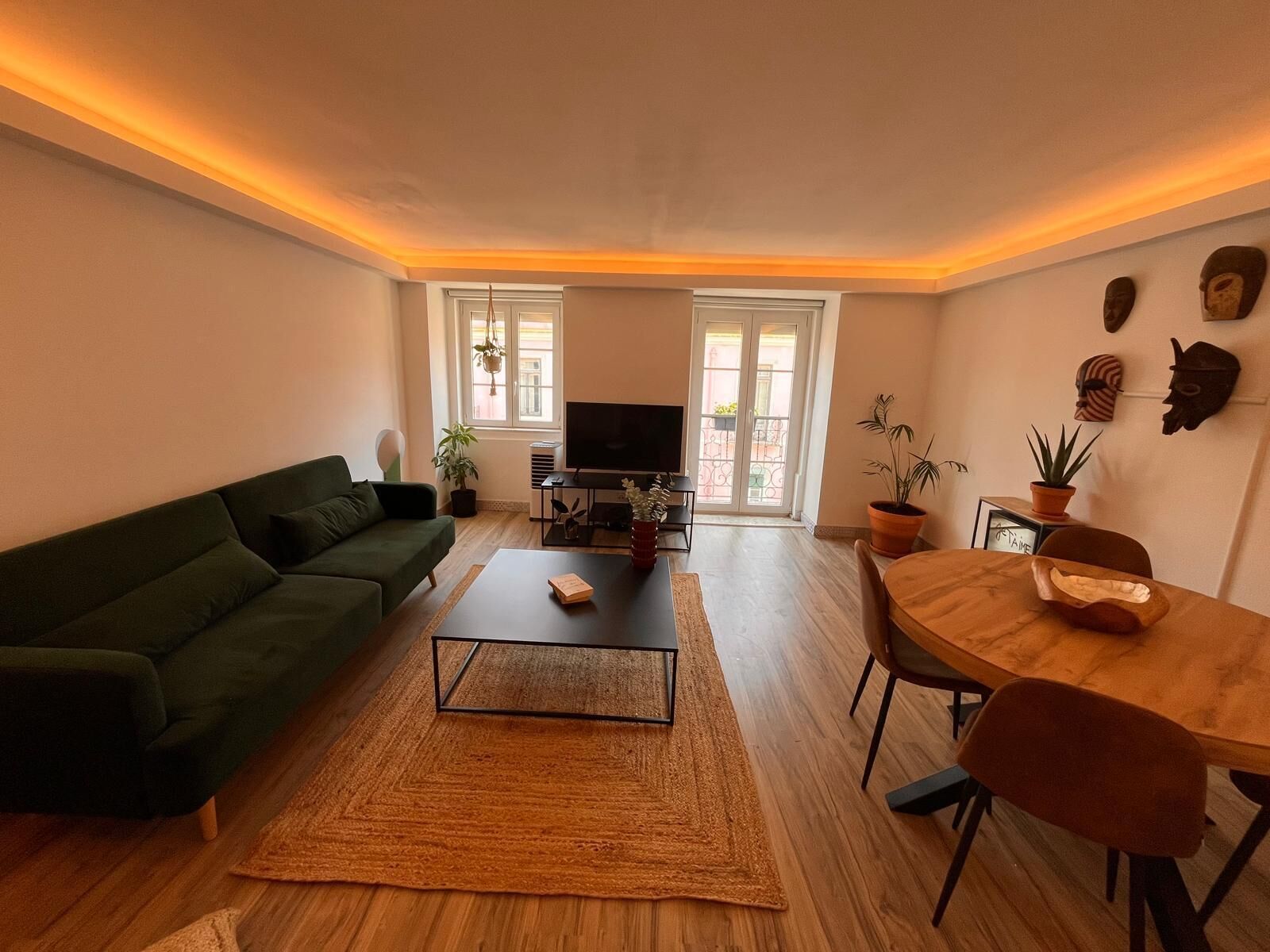 Un salon avec un canapé vert, une table basse, un téléviseur et un coin repas comprenant une table et des chaises.