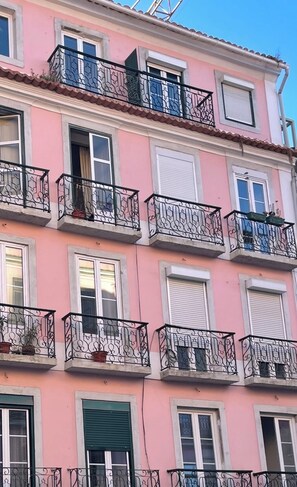 Ein mehrstöckiges Gebäude mit Balkonen, Fenstern mit Fensterläden und einer rosafarbenen Fassade.