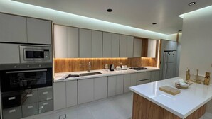 A modern kitchen with built-in appliances, a central island, and a wooden accent wall. - حياة ريفية في وسط مدينة الباحة، شاليه فيلا دورين بتأثيث فندقي فاخر وجلسة خارجية (Al Bahah)