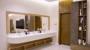 A modern bathroom with a long vanity, a large mirror, and a wooden cabinet with decorative items. - حياة ريفية في وسط مدينة الباحة، شاليه فيلا دورين بتأثيث فندقي فاخر وجلسة خارجية (Al Bahah)