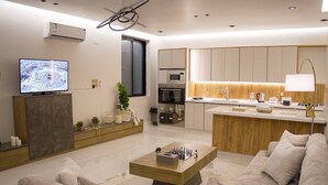 A modern living room with a sofa, a coffee table, a TV, and a kitchen area with a microwave. - حياة ريفية في وسط مدينة الباحة، شاليه فيلا دورين بتأثيث فندقي فاخر وجلسة خارجية (Al Bahah)