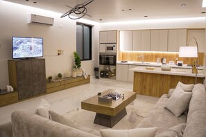 A modern living room with a sofa, a coffee table, a TV, and a kitchen area with a microwave. - حياة ريفية في وسط مدينة الباحة، شاليه فيلا دورين بتأثيث فندقي فاخر وجلسة خارجية (Al Bahah)