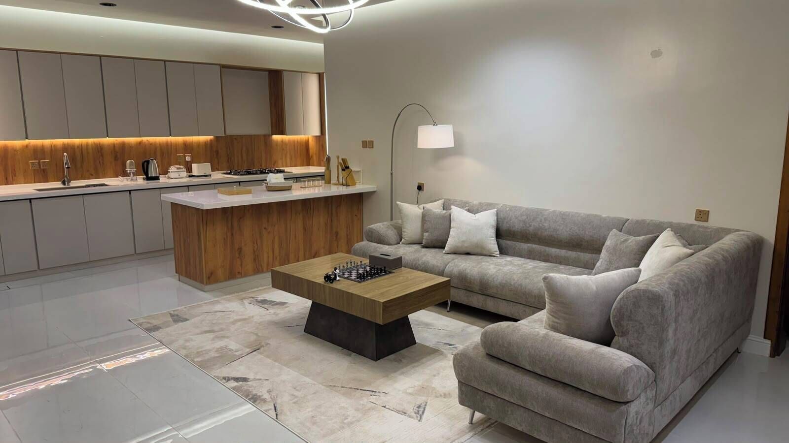 A modern living room with a sofa, coffee table, and a kitchen area with a wooden accent wall.