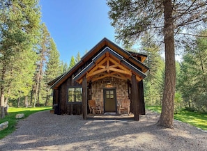 A rustic cabin with a stone facade, wooden beams, and a porch with two chairs.