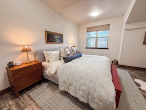 A bedroom with a bed, bedside table, lamp, and a window with a view.