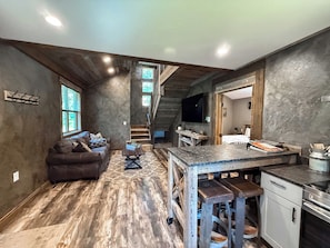A spacious living area with a sofa, coffee table, and a kitchen area with a counter and stools.