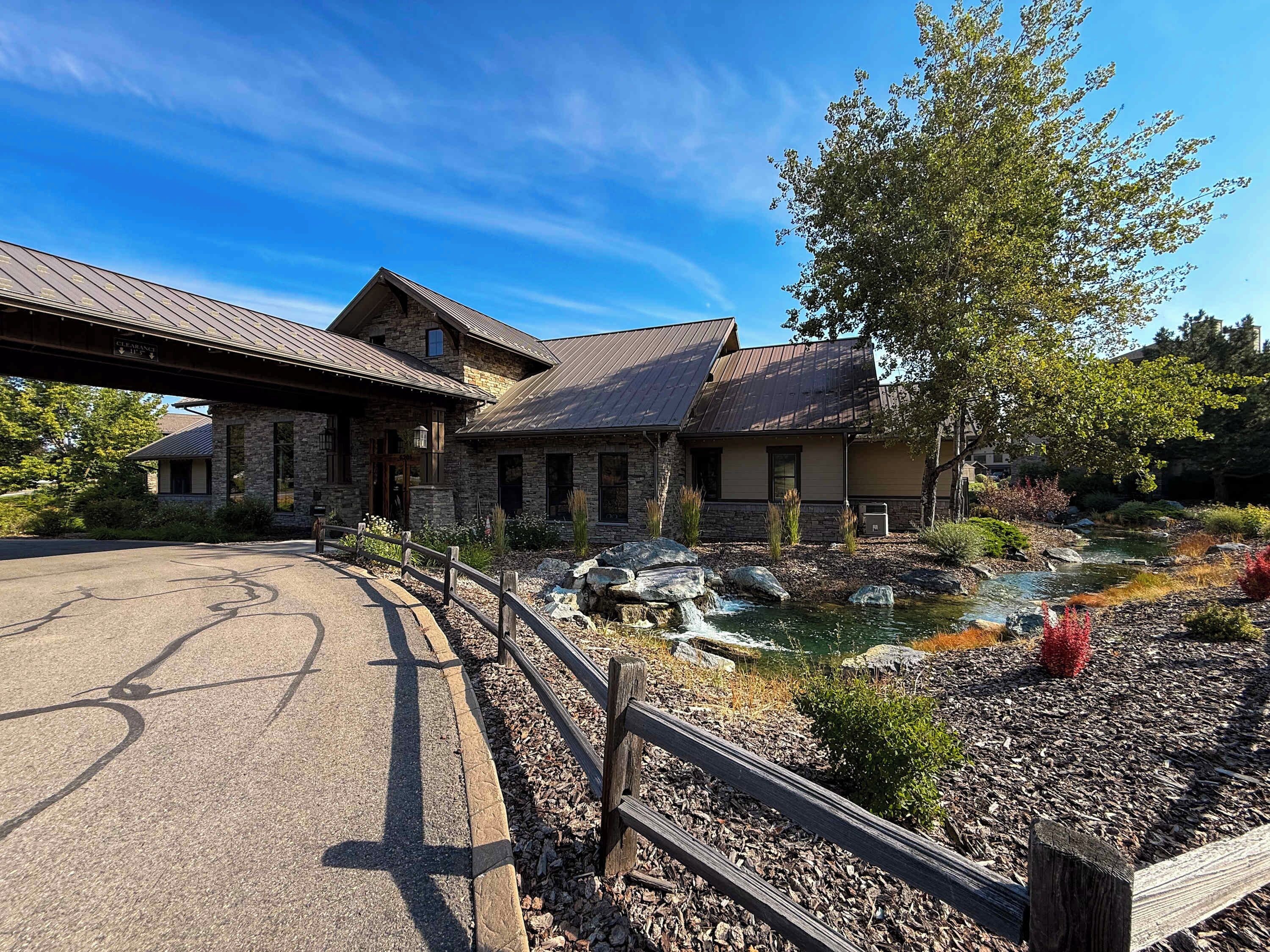 A stone building with a metal roof, a paved driveway, and a landscaped area with a small water feature.