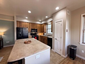 A modern kitchen with wooden cabinets, a black refrigerator, a microwave, and a sink. - Long Term | 1 BR/1.5BA | Communal Pool & Hot Tub (Whitefish)
