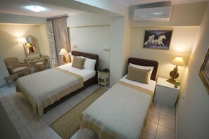 Quarto de hotel com duas camas, uma escrivaninha, uma cadeira, mesa de cabeceira com abajur e um quadro na parede.