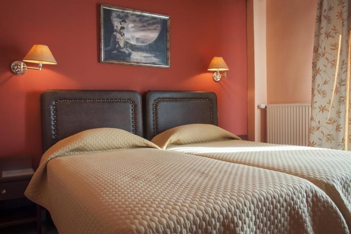 Uma cama de casal com colcha texturizada, duas luminárias fixadas na parede e um quadro emoldurado sobre a cama.
