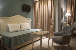 Quarto de hotel com uma cama, uma mesinha, uma cadeira, um abajur e um espelho.