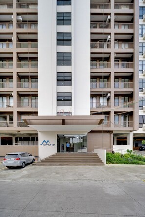 A multi-story residential building with a central entrance, a parking area, and a sign indicating 'MACTAN PLAINS RESIDENCES'. - Nagi 凪 Quiet Studio Stay with AC (Lapu-Lapu)