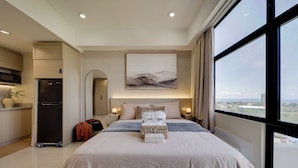 Een moderne hotelkamer met een groot bed, uitzicht op de stad en een kitchenette.