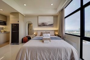 A modern hotel room with a large bed, a view of the city, and a kitchenette. - Nagi 凪 Quiet Studio Stay with AC (Lapu-Lapu)