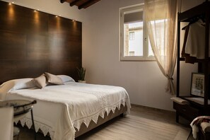 A bedroom with a large bed, a bedside table, a nightstand, a window with curtains, and a headboard.