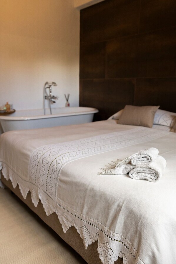 A hotel room with a bed, a large dark headboard, a white bathtub, and a towel on the bed.
