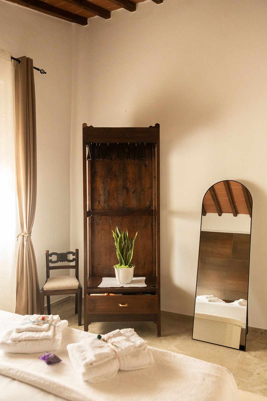 Ein Zimmer mit einem Bett, einem Nachttisch mit Pflanze, einem Stuhl und einem Spiegel.