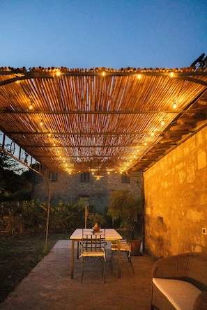 An outdoor patio with a bamboo pergola, a table, chairs, and a potted plant.